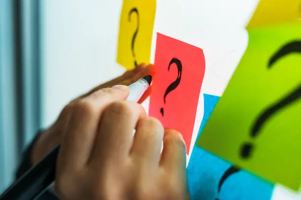 Businesswoman writing question marks on colorful sticky note paper on office whiteboard, selective focus