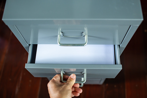 Woman's hand opening drawer of silver grey metal colour filing cabinet, White papers for write letter, Administration and storage, Close up shot, Selective focus, Stationery, Business concept