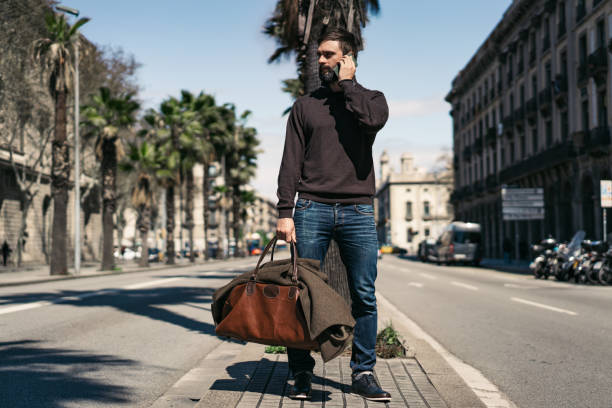 istock Attractive bearded man holding travel bag and using mobile mobile phone outside. Blurred background. 1141694475