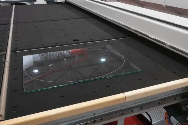 piece of transparent glass lays on industrial CNC computer remote controlled glass cutter water-jet or laser system