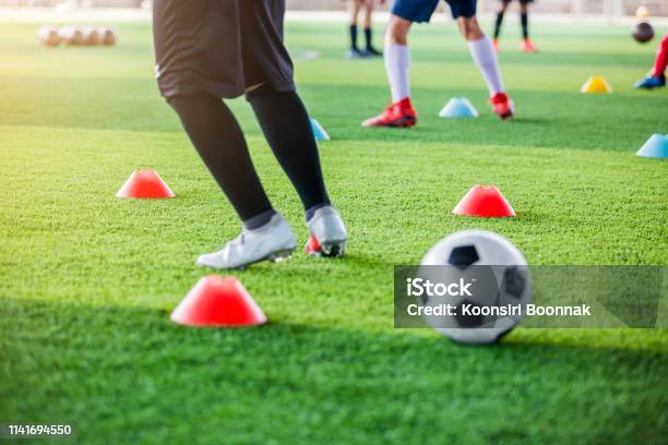 Selective Focus To Red Marker Cones With Blurry Soccer Ball And Kid Soccer Player Jogging And Jump Between Cone Markers Stock Photo - Download Image Now