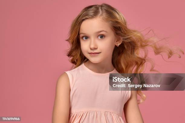 Little Girl With A Blond Curly Hair In A Pink Dress Is Posing For The Camera Stock Photo - Download Image Now
