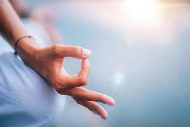 Close up image of woman’s hands in lotus position by the lake