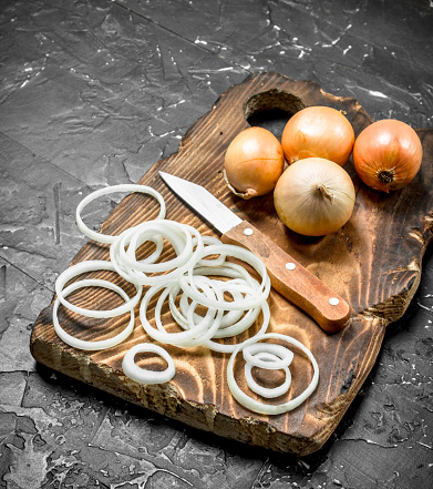 Rings of onions on a cutting Board with a knife. On rustic background