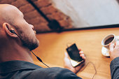 The man in headphones using mobile phone, sitting with coffee at cafe