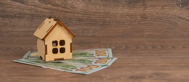 house mortgage concept with wooden house model and 100 dollar banknotes