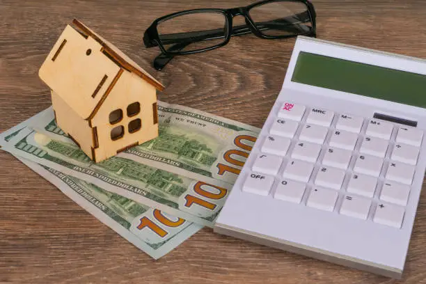 house purchase concept with wooden house model calculator and 100 dollar banknotes