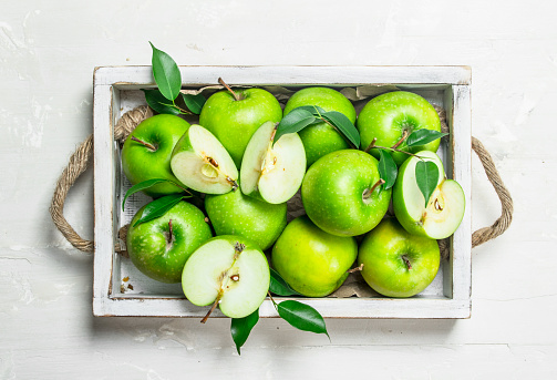 Green apples in a wooden tray. On white rustic background .