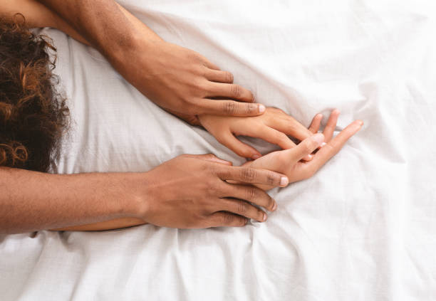 ベッドの上でセックスをしている男と女の手 - 官能 ストックフォトと画像