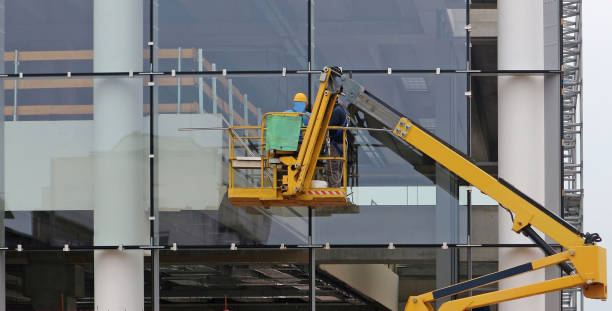 チェリーピッカー上の労働者。彼らは改装中の建物のガラスのファサードを仕上げている - steel construction site construction glass ストックフォトと画像