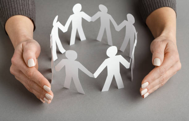 istock Businessperson's hand protecting paper cut out figures 1141705929