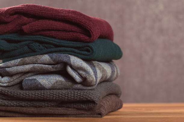 istock Bunch of knitted warm pastel color sweaters with different knitting patterns folded in stack on brown wooden table, grunged texture wall background 1141706456