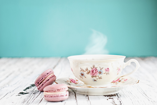 Antique Bavaria Winterling footed tea cup from the 1950's with pink macarons on a rustic white table against a teal background..
