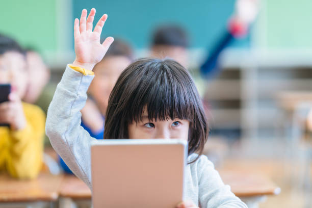 Little cute girl holding digital tablet and raising hand in classroom A little cute girl is holding a digital tablet and raising her hand in classroom. child japanese culture japan asian ethnicity stock pictures, royalty-free photos & images
