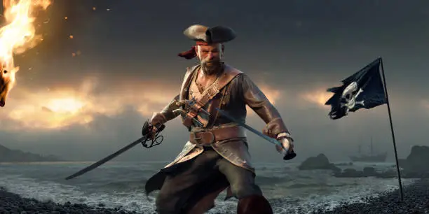 Fierce looking male pirate standing, holding a cutlass and sword with arms out ready for combat. The pirate is dressed in leather tricorn hat, frock coat, waist cost and shirt, carrying two pistols. He stands on a stony beach full of pebbles, near a fire and jolly roger flag at sunset.