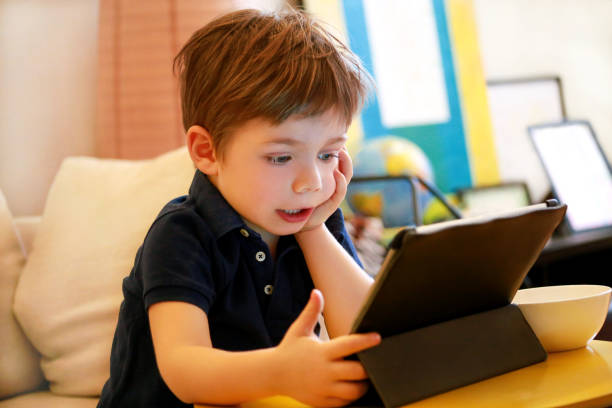 istock Child using tablet pc on bed at home. Cute boy on sofa is watching cartoon, playing games and learning from laptop. Education, fun, leisure, happiness, modern computer technology and communication. 1141721821