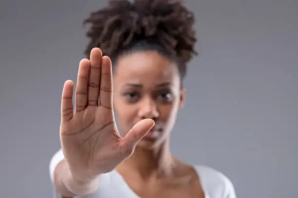 Attractive young African woman giving a halt or stop gesture with focus to the palm of her hand over a grey studio background
