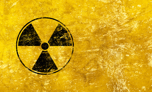 Black radioactive hazard warning sign painted over grunge yellow background with copy space