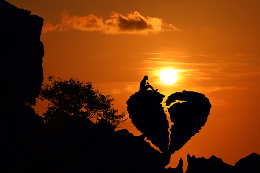 Couple on the broken heart shape rock on the mountain with red sky sunset.Silhouette Valentine background concept.