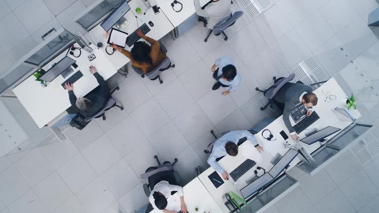 Aerial Top Down Drone Shot of Big Busy Corporate Office with Tow Rows off Businessmen and Businesswomen Working on Desktop Computers. Bright Open Space Office with Businesspeople and Salespeople