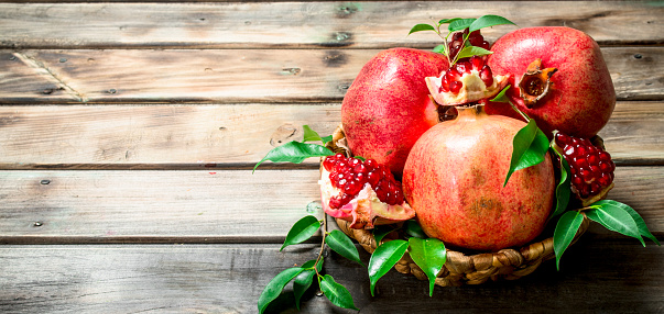 Fresh pomegranates with leaves in a basket. On wooden background