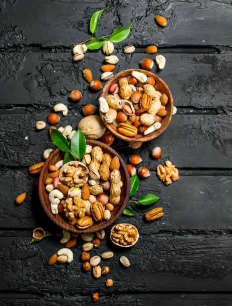 Assortment of different types of nuts in bowls. On black rustic background.