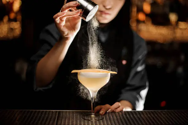 Female bartender pours an alcohol light brown cocktail with sour mix in glass