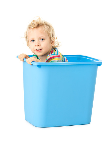 Funny picture of small happy boy isolated on white . He is 30 months old. He is sitting in blue plastic box