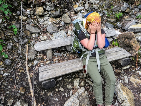 A close up of an exhausted female hiker sitting down on a bench with her hands over her face.  She is tired from a long day of hiking the Berg Lake trail in Mount Robson Provincial Park, Canada