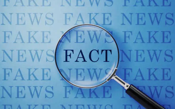 Photo of Fake News And Fact Concept - Magnifier And Fake News Text On Blue Background