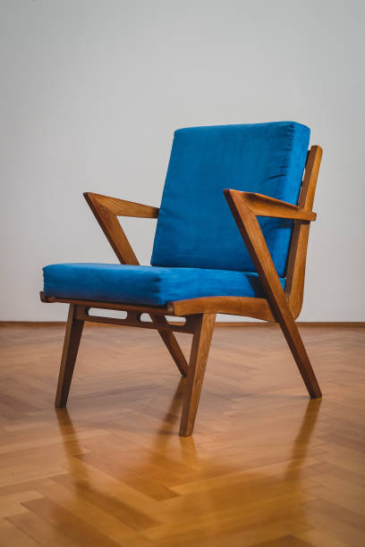 Wooden chair with blue padding, standing on a wooden floor and in front of a white wall. Retro design.