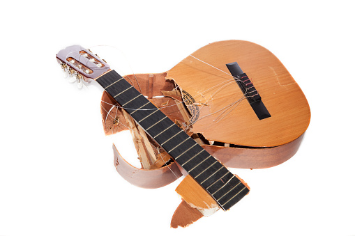 Broken acoustic guitar smashed to pieces. Frustrated angry musician. Demolished classical musical instrument destroyed by a music student guitarist. Isolated against white background.