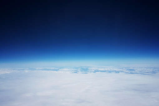 Low earth orbit - View of white clouds and mountains during the flight to the low orbit of the Earth, at the top of the blue sky and space