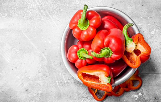 Pieces of sweet pepper and whole red peppers in the bowl. On rustic background