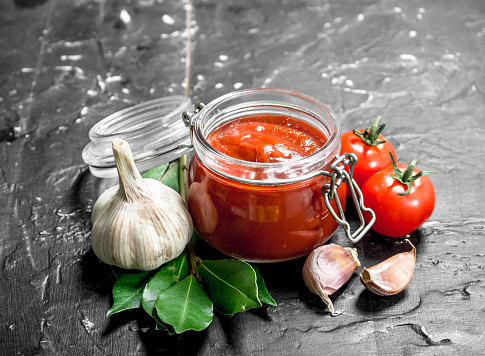 Tomato sauce in bowl with garlic and Bay leaf. On black rustic background