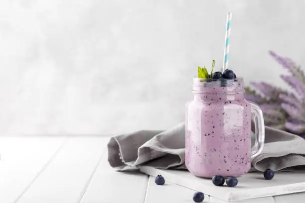 Blueberry smoothie in a glass jar garnished with berries, horizontal copy space