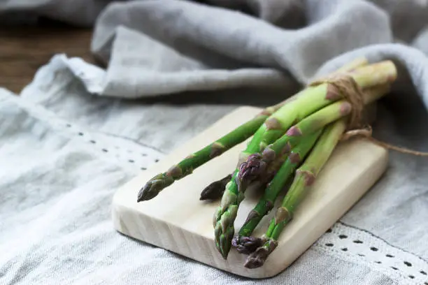 Photo of A bunch of fresh asparagus, tied with twine, against a linen tablecloth. Rustic style.