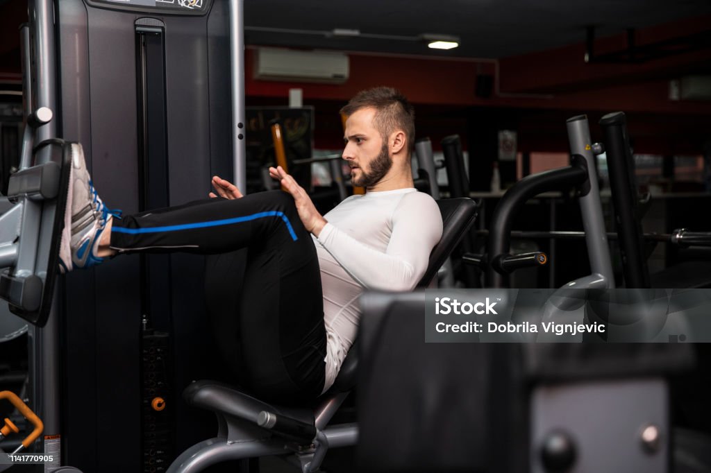 Fitness and Sport. Athletic man is doing exercises on legs in gym. Fit man is  training legs on leg press machine in the gym.Sport training indoors. Sport concept, healthy lifestyle, gym concept. 30-39 Years Stock Photo