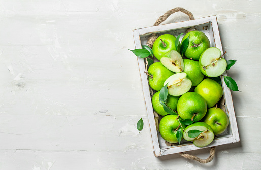 Green apples in a wooden tray. On white rustic background .