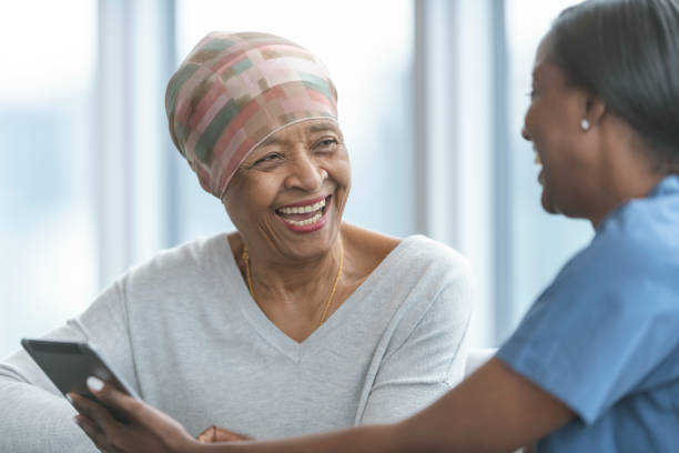 Senior woman with cancer reviews test results with female doctor A woman with cancer is meeting with her doctor. Both individuals are of African descent. The doctor is showing the patient test results on an electronic wireless tablet. They both smile as the doctor gives good news regarding the patient's treatment. brest cancer hope stock pictures, royalty-free photos & images