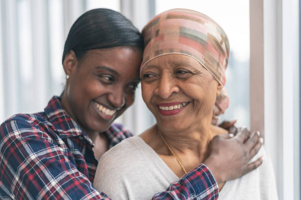 Courageous woman with cancer spends precious time with adult daughter A black senior woman with cancer is wearing a scarf on her head. Her adult daughter is giving her a hug. Both women are smiling with gratitude and hope for recovery. food chain stock pictures, royalty-free photos & images