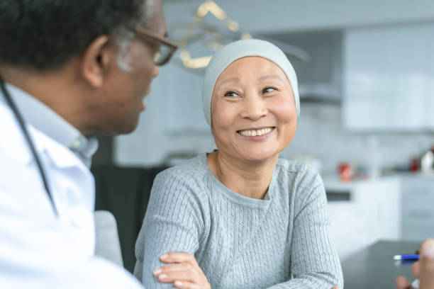 Beautiful Korean woman with cancer smiles at doctor A Korean woman with cancer is meeting with her doctor. Chemotherapy treatment is going well. The patient is smiling at her doctor as he shares with her positive news. chronic illness photos stock pictures, royalty-free photos & images
