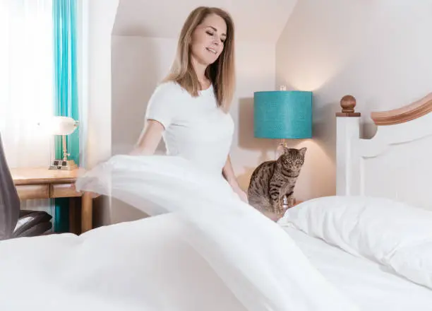 A blonde woman in blurred motion making her white linen bed. Teal and orange colors.