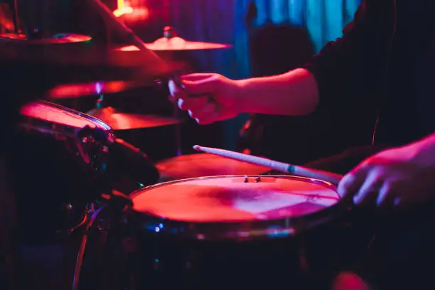 Photo of Drummer playing drum set at concert on stage. Music show. Bright scene lighting in club,drum sticks in hands.