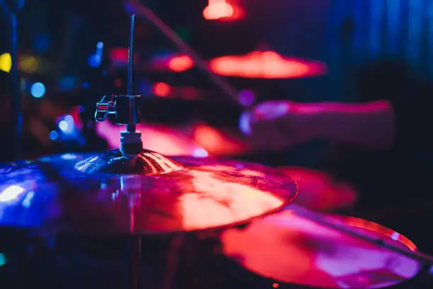 Photo of Drummer playing drum set at concert on stage. Music show. Bright scene lighting in club,drum sticks in hands.