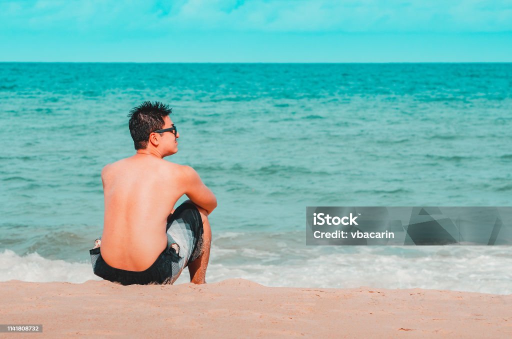 Man seated on the sand of the beach Man seated on the sand of the beach staring the sea. Cyan and orange tones. Photo at Praia de Tabatinga 2, Conde PB Brazil. João Pessoa Stock Photo