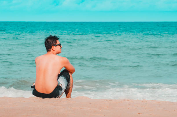 Man seated on the sand of the beach stock photo