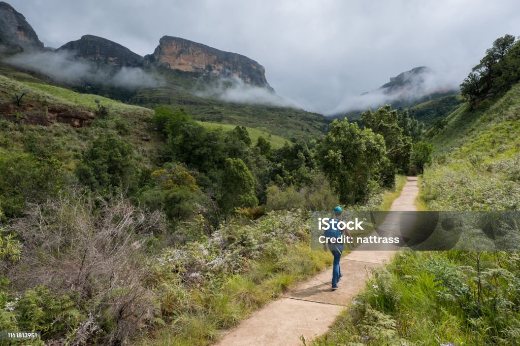 Female hiker enjoys hiking in the mountains A young female hiker with a backpack hikes along a well marked footpath in the Drakensberg mountains near Kwazulu Natal Drakensberg Mountain Range Stock Photo
