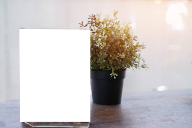 Mock up white Label for blank menu frame in restaurant cafe with plant pot. Stand booklet sheets paper tent card on table cafeteria display your product  background insert  text of customer.
