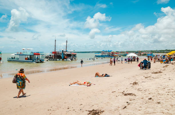 Joao Pessoa - PB, Brazil - February 24, 2019: Local people and tourists at Tambau beach (praia de tambau) on a sunday enjoying the beach on a beautiful sunny day. Touristic Catamaran boats on the sea.